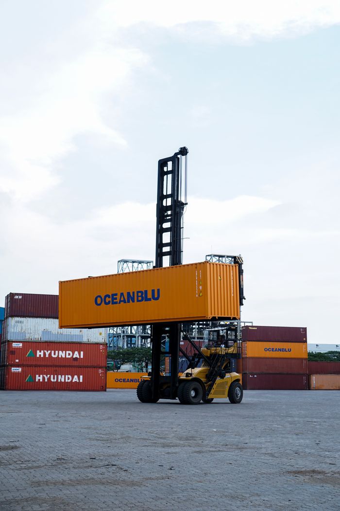 Forklift handling container in bustling Jakarta port with clear skies.