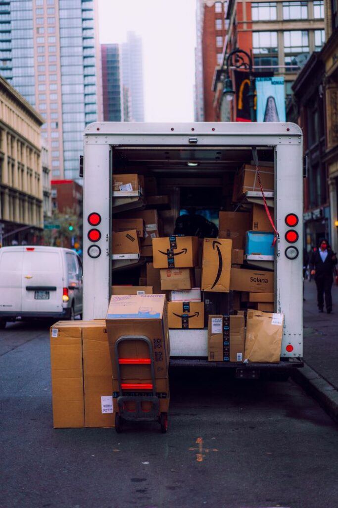 A delivery truck overflowing with cardboard boxes parked on a busy city street.