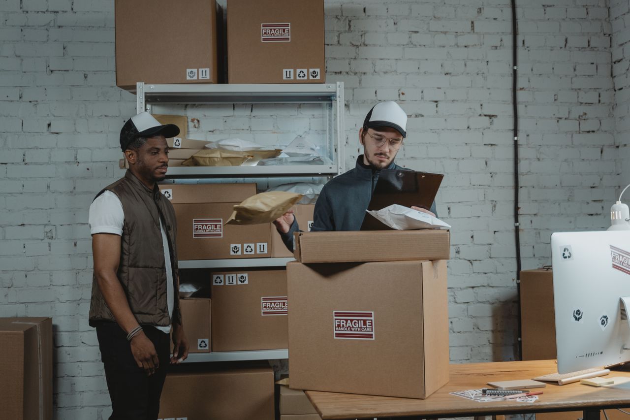 Two workers in a warehouse handling and checking fragile labeled packages before shipping.